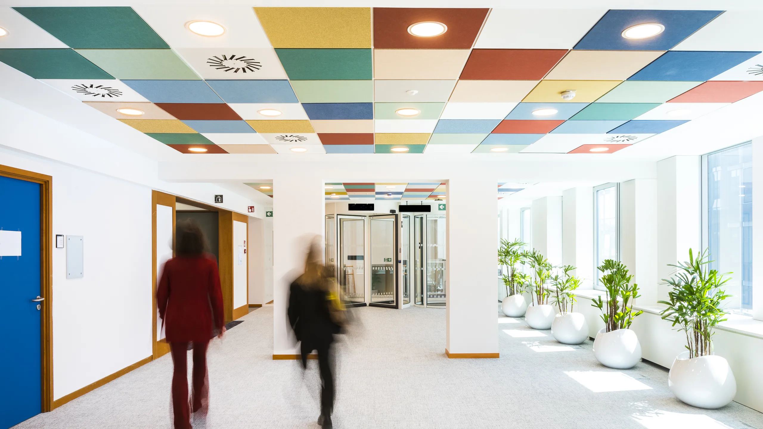 Office corridor with colourful checked acoustic ceiling tiles arranged in a geometric pattern above the walkway.