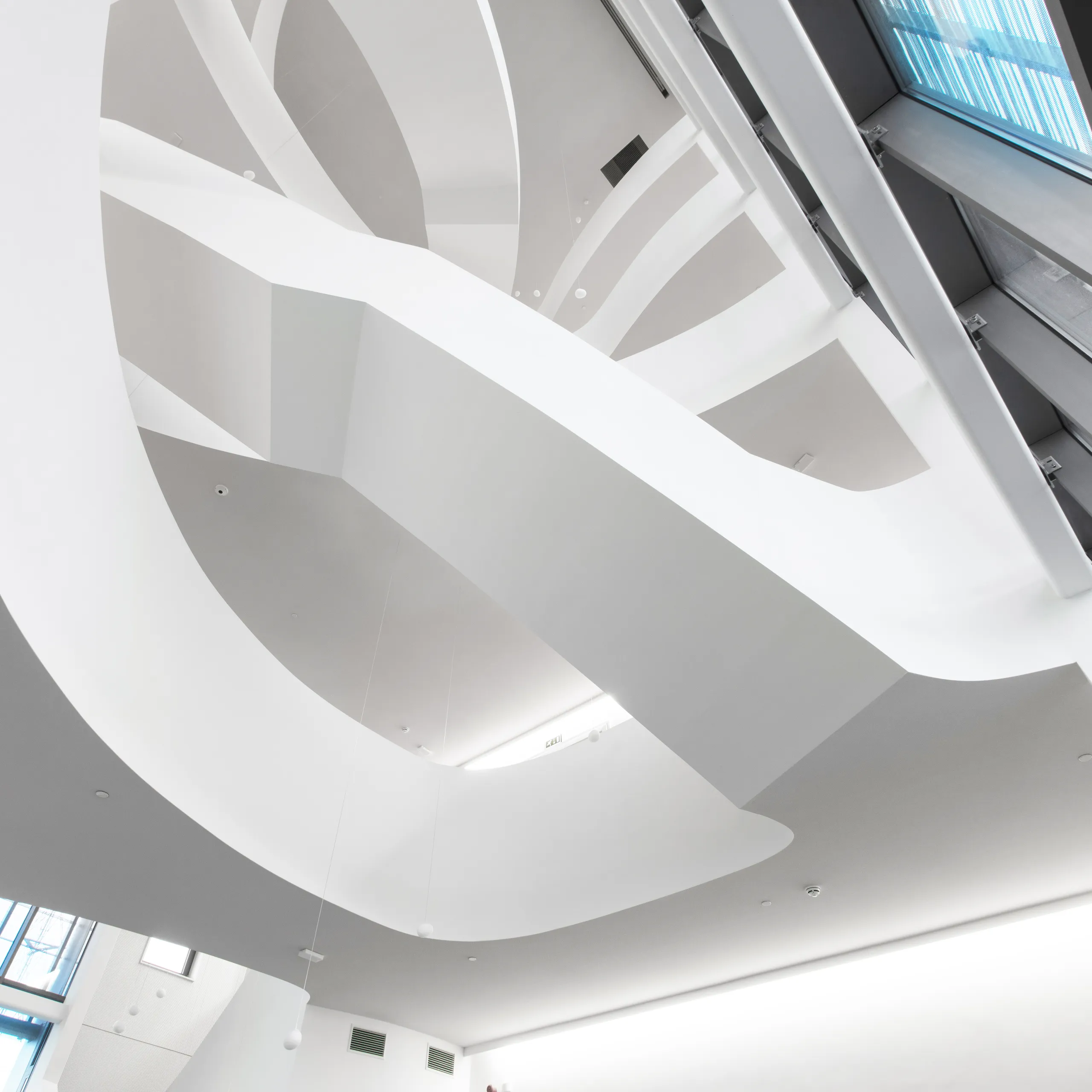 Contemporary multi-storey atrium showcasing a monolithic acoustic ceiling with sculptural white curves, integrated lighting, and tall skylights illuminating the lobby
